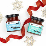 Two glass jars of Red Pepper Jam and Strawberry Rhubarb Jam with red ribbons and wooden snowflakes.