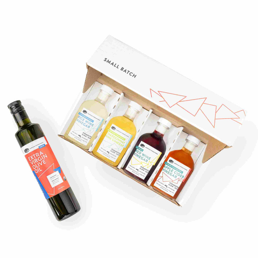 A gift set containing a bottle of American Vinegar Works Extra Virgin Olive Oil alongside a box featuring four small-batch vinegars: Rice Wine, Chardonnay Wine, Red Wine, and Apple Cider Vinegar.