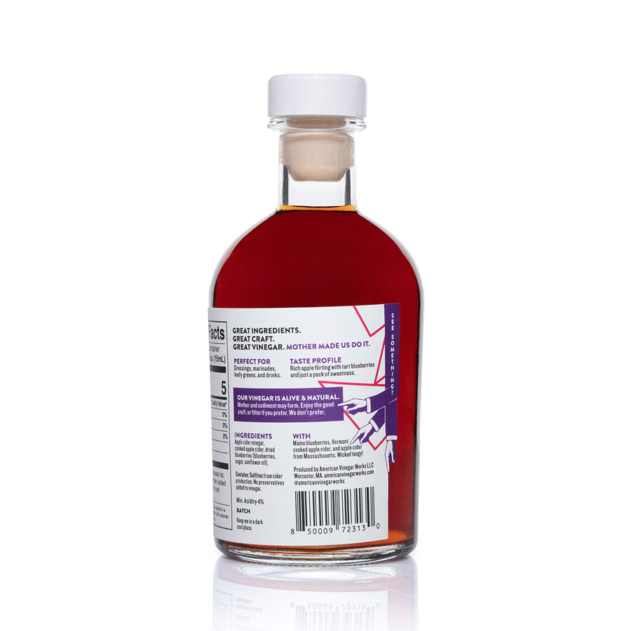 A detailed back view of an 8.5 fluid ounce bottle of American Vinegar Works Blueberry Apple Cider Vinegar, showcasing an ingredients list with dried blueberries, a taste profile described as rich apple flirting with tart blueberries, and the nutrition facts panel against a white background.