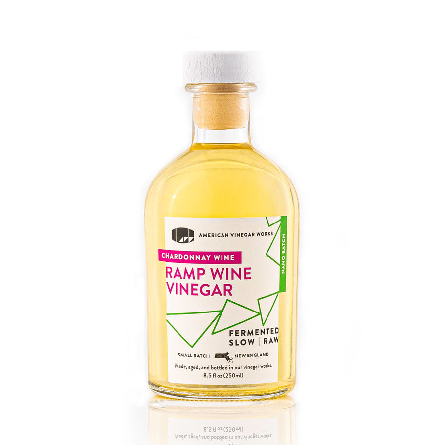 The front view of an 8.5 fluid ounce nano batch bottle of American Vinegar Works Chardonnay Wine Ramp Wine Vinegar, showcasing a pale yellow liquid and a white label with bright pink and green accents against a clean white background.