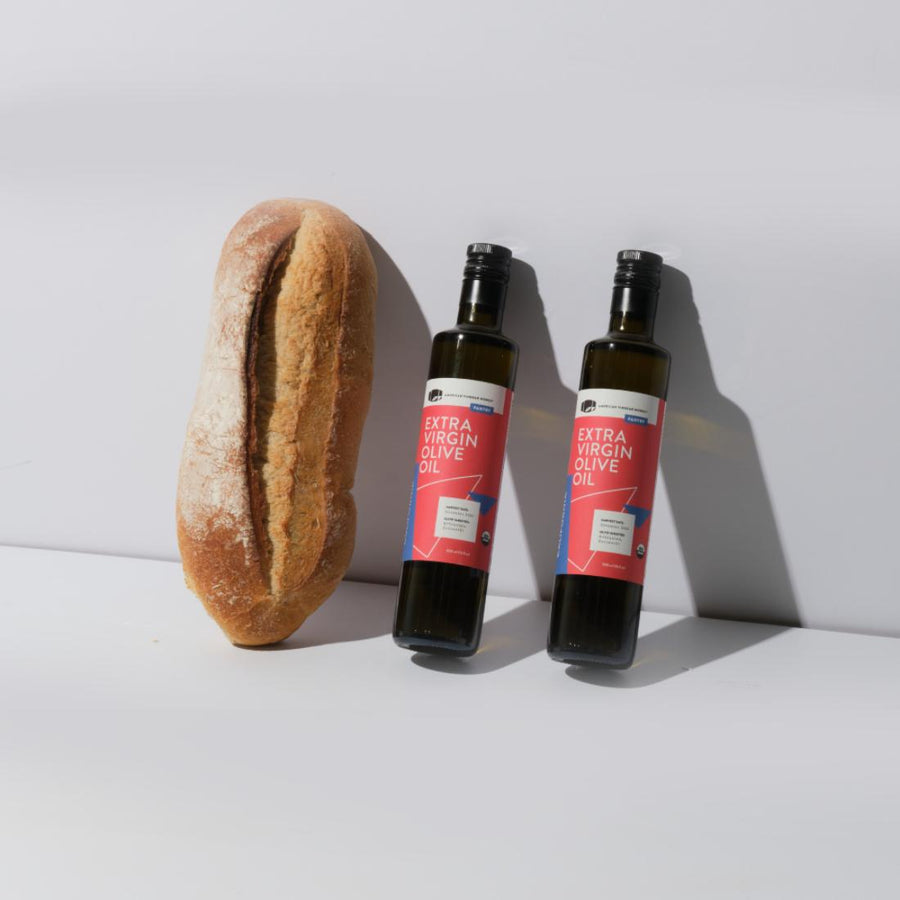 Two bottles of American Vinegar Works California Organic Extra Virgin Olive Oil with a loaf of bread