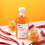 Hot Honey Vinegar glass bottle surrounded by honey combs and red peppers