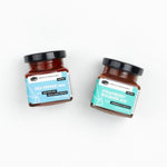 A square-cropped top-down view of two jars from the American Vinegar Works Jam Gift Set, featuring Red Pepper Jam and Strawberry Rhubarb Jam side by side against a white background.