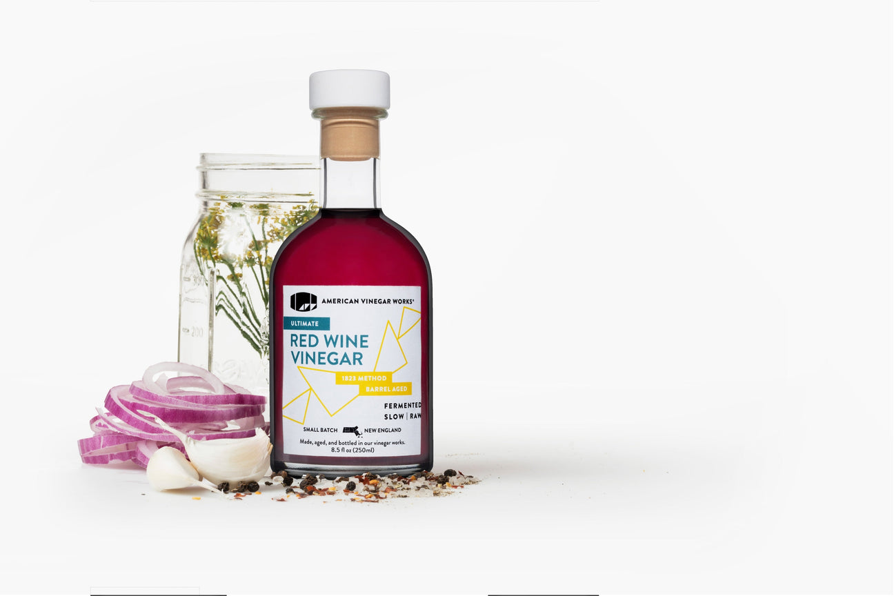 Bottle of red wine vinegar with pickling jar, onion slides, garlic, and spices.  Photo taken as head on view