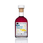 The front view of an 8.5 fluid ounce bottle of American Vinegar Works Ultimate Red Wine Vinegar, showcasing a deep red liquid and a white label with teal and yellow accents against a clean white background.