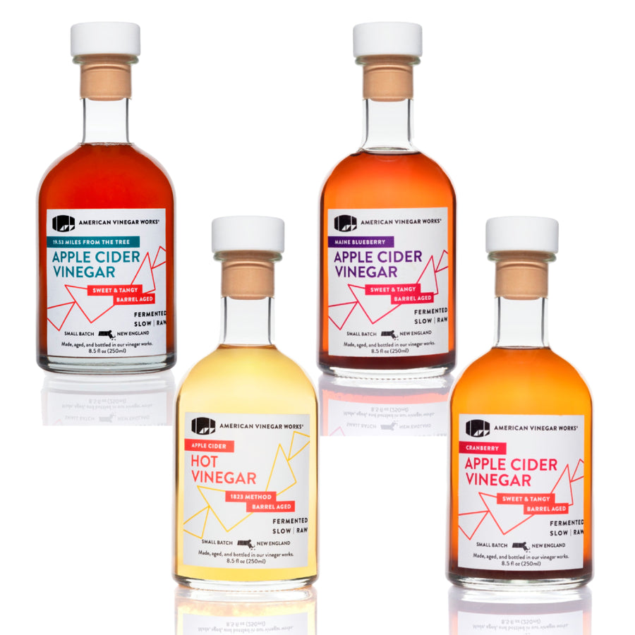 Apple cider vinegar four-bottle collection on reflective surface — artisanal apple cider vinegar